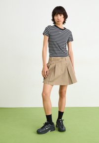 Striped black and white T-shirt, beige pleated skirt with button detail, black sneakers, and crew-length black socks on green floor.