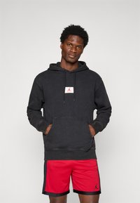 Zwarte hoodie met voorzak en wit/rood logopatch, gecombineerd met rode sportshorts met zwarte details en logo.