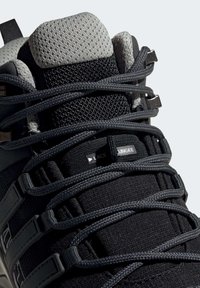 Gros plan sur une chaussure de sport noire et grise avec des lacets épais et texturés passés dans des boucles étiquetées "LACE BUNGEE".