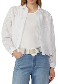 Witte oogjes blouse met een kraag, voorzien van geborduurde patronen en een gegolfde zoom, gecombineerd met een witte gevlochten riem en denim jeans.