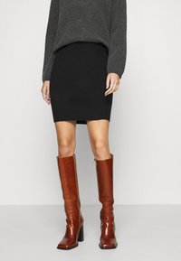 Svart stickad minikjol i kombination med glansiga bruna knä-höga stövlar med en kraftig klack och sidodragkedja. Grå långärmad tröja ovanpå.