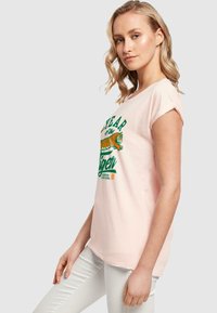 Lichtroze T-shirt met korte mouwen, gemaakt van katoen. Heeft een bedrukte groene en oranje tijgerontwerp met de tekst "Jaar van de Tijger."