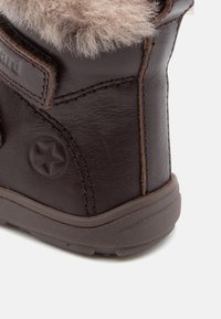Brun läderstövel med mjuk beige pälsfoder upptill, rund stjärnlogotyp på sidan och texturerad gummisula.