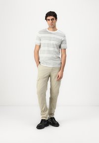 Light gray striped t-shirt with short sleeves, paired with beige cargo pants. Black shoes complete the outfit. Minimalist design and fit.