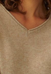 Maglione beige a scollo a V realizzato in morbido tessuto a maglia testurizzato, caratterizzato da un motivo sottile e una vestibilità comoda attorno al collo e alle spalle.