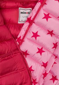 Punainen täytepuku, jossa on vaaleanpunaista tähdenkuvioista vuoria ja vetoketjukiinnitys. Tunnuksessa lukee koko 4-5 vuotta, valmistettu Myanmarissa.