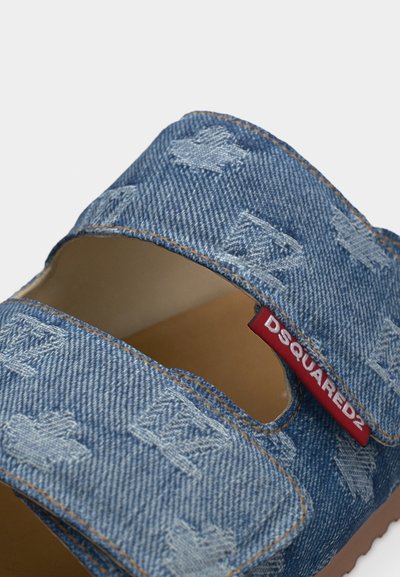 Sangles de sandale en denim bleu avec motifs brodés et une étiquette en tissu rouge affichant le nom de la marque "DSQUARED2".