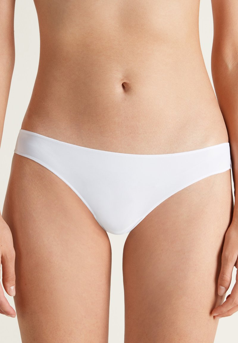 Culottes de bikini blanches avec une texture lisse, un design taille basse et une large ceinture élastique. Style simple et minimaliste sans motifs.