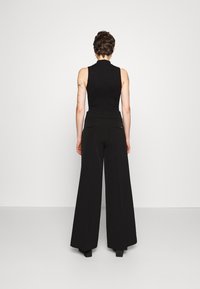 Černý pletený bezramínkový top s vysokým límcem, doplněný širokými černými kalhotami s hladkou texturou a minimalistickým designem.