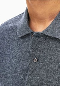 Tmavě šedá polo košile z texturované látky s klasickým límcem a jedním knoflíkem, těsně vyříznutá v oblasti krku.