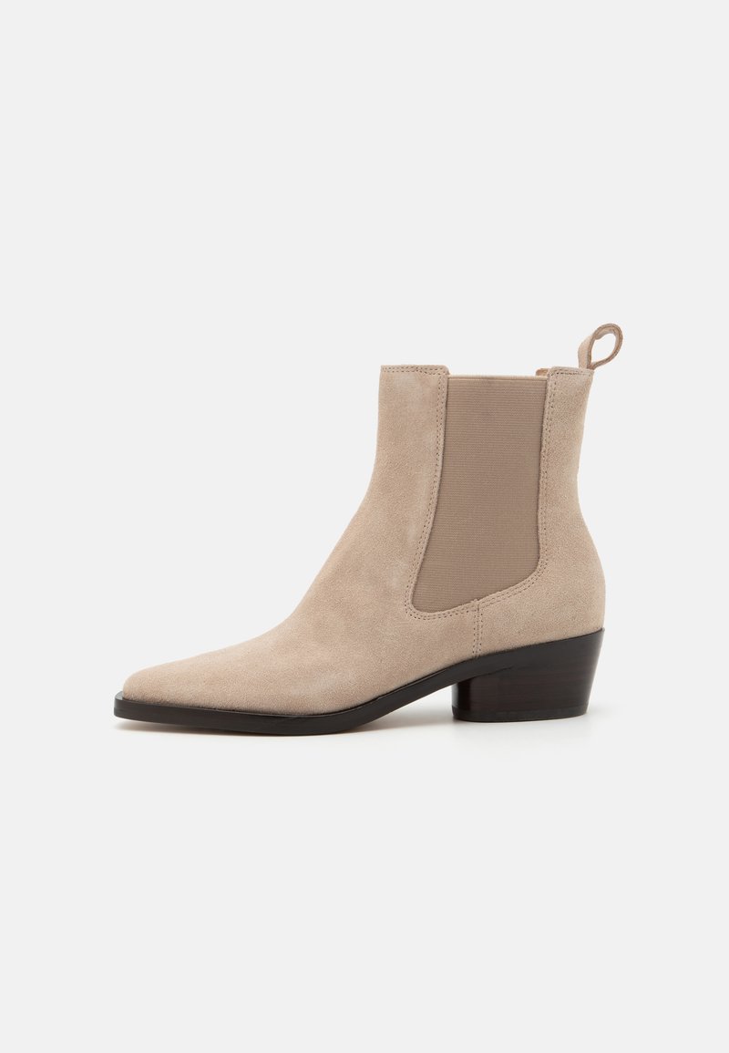 Beige semsket ankelstøvlett med spiss tå, elastiske sidestrimler og en liten blokk hæl. Har en pull-tab bak for enkel påkledning.