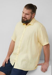 Korte mouwen gele linnen shirt, met knoopsluiting aan de voorkant, textuurstof, afgeronde zoom, gedragen met marineblauwe shorts. Geen graphics of patronen.