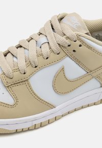 Baskets crème et bleu clair avec des lacets plats, en cuir, logo en forme de virgule de la marque, et semelle en caoutchouc texturée.