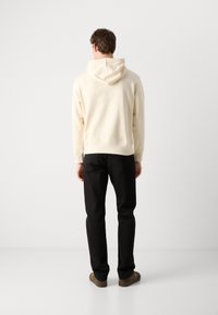 Sudadera capucha beige claro con una textura suave, combinada con pantalones negros y zapatos marrones. Sin logotipos ni patrones visibles.