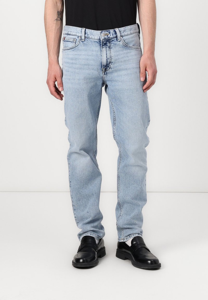 Jeans de mezclilla azul claro con costuras contrastantes, diseño de cinco bolsillos y corte recto, combinados con mocasines negros.