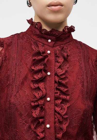 Bordová čipková blúzka so stojatým volánovým golierom, vodorovnými pruhmi a perlovými gombíkmi na prednej strane, s precíznymi kvetinovými vzormi.