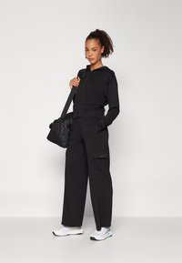 Black zip-up hoodie with a spacious pocket, paired with black wide-leg pants featuring cargo pockets. White sneakers and a black bag complete the look.