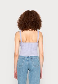 Top cropped em lavanda com nervuras, alças finas e um design ajustado. O material é elástico e apresenta uma cintura sem costura. Jeans de corte relaxado visíveis na parte inferior.