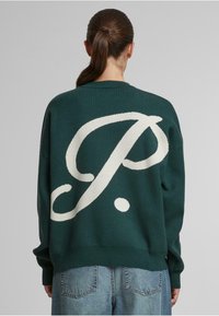 Grüner Strickpullover mit einem großen weißen Buchstaben "P" und Punktdesign auf der Rückseite. Bequeme Passform mit gerippten Bündchen und Saum.
