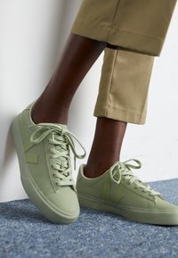 Baskets en cuir vegan vert clair avec des bouts arrondis, des lacets plats et une semelle en caoutchouc, arborant un logo subtil et des panneaux latéraux texturés.