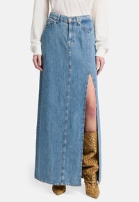 Gonna maxi in denim, blu chiaro, con spacco frontale e design classico a cinque tasche. Abbinata a stivali al ginocchio marroni con pois.