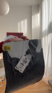 Fekete ruha átlátszó műanyag csomagolásban, rajta S méret és ápolási utasítások. Kiemelkedő a sima textúrája és egyszerű dizájnja.