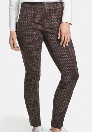 Gros plan d'une personne portant un pantalon moulant sombre à motif géométrique discret et des baskets blanches, debout les mains détendues.
