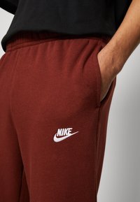 Pantalones de chándal burdeos de tejido suave, con cintura elástica y bolsillos laterales. Logo de Nike en blanco bordado en la parte frontal.