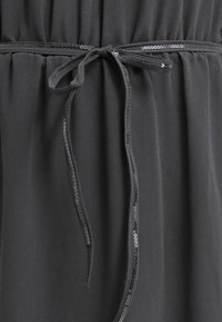 Robe noire en jersey avec une taille froncée dotée d'un lien, accentuée par une bordure en sequins le long de l'encolure et de la taille.