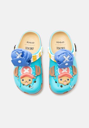 Lyseblå Crocs med tegneseriefigurers ansigter med brune gevirer, lyserøde hatte og påsyede blå stofflapper med hvide X-mærker.