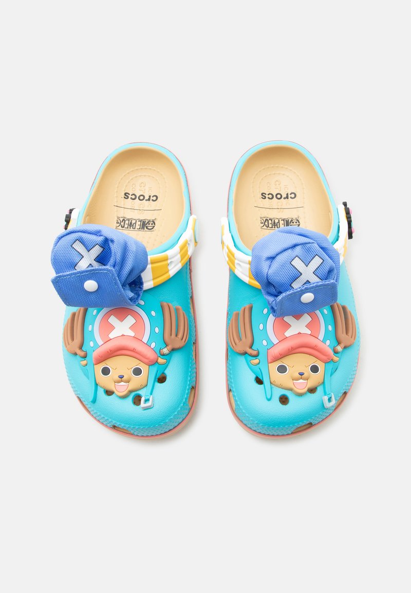 Φωτεινά μπλε Crocs με πρόσωπα κινούμενων σχεδίων με καφέ κέρατα, ροζ καπέλα και συνδεδεμένα μπλε υφασμάτινα καλύμματα με λευκές σημαίες X.