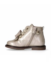 Stivaletti alla caviglia in pelle verniciata beige con punta arrotondata, lacci frontali, fiocco decorativo e zip laterale per un facile utilizzo. Suola in gomma marrone.