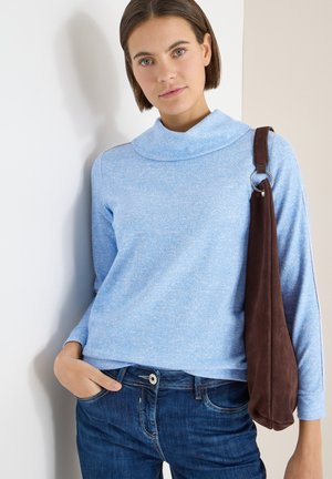 Suéter azul claro acanalado con cuello doblado, combinado con jeans azul oscuro. Un bolso de ante marrón cuelga del hombro, añadiendo contraste.