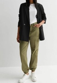 Sort blazer over en hvid t-shirt, matchet med olivengrønne cargo-bukser med elastiske manchetter. Hvide sneakers fuldender outfittet.