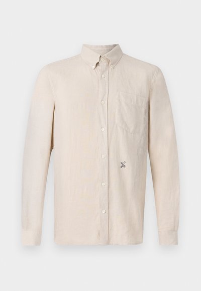 Chemise à manches longues beige clair avec col, devant à boutons, poche poitrine simple et motif brodé discret sur le côté gauche.
