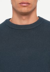 Navy ribbed sweater with a round neckline. The fabric has a textured, knitted appearance, showcasing fine vertical lines.