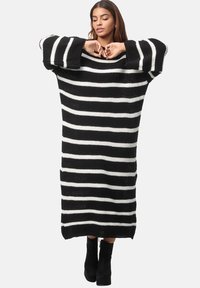 Übergrößes, schwarz-weiß gestreiftes Strickkleid mit weiten Ärmeln, geripptem Material und lockerem Schnitt, das bis zur Mitte der Waden reicht.