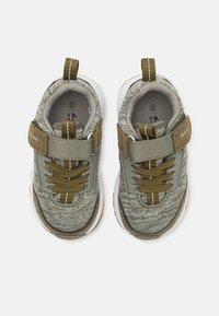 Barnestørrelse grønne og brune sportssko med hvite såler, en borrelåsrem, snører og drahåndtak, vist ovenfra på en hvit bakgrunn.