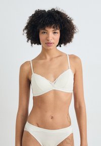 Hvit bralette med blonder, justerbare stropper og mykt stoff, med trekantet fasong og subtil tekstur. Matchende bikinitruser.