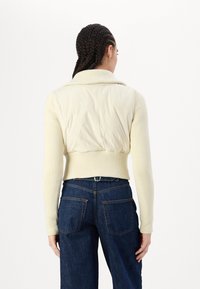 Maglione crema tagliato con texture a coste e collo a scialle, abbinato a jeans blu scuro con due tasche posteriori e una vestibilità classica.