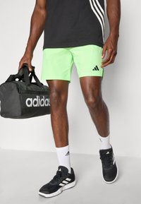Shorts de sport verts, sac de sport Adidas noir, chaussures noires avec accents blancs et chaussettes assorties. Tenue de sport simple et fonctionnelle.