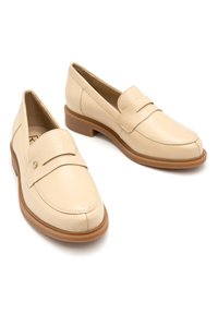 Mocassini in pelle beige con punta tonda, caratterizzati da un dettaglio cucito e una piccola fascia sulla parte superiore. Suola piatta color marrone chiaro.