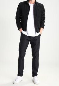 Sort bomberjakke, hvid t-shirt, mørke bukser og hvide sneakers. Jakken har en lynlåslukning og ribbede manchetter. Enkel og moderne stil.