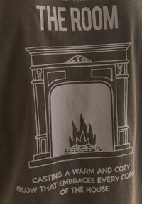 Graphic showing a fireplace design in white on a dark fabric, featuring a stylized flame and text below stating "CASTING A WARM AND COZY GLOW."