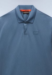 Hellblaues Poloshirt aus weichem Baumwollmaterial, mit einem klassischen Kragen, einer Knopfleiste mit drei Knöpfen und einem dezenten, geprägten Logo auf der Brust.