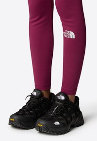 Scarpe da outdoor nere con pannelli in rete, suola Vibram e logo The North Face. Abbinati a leggings aderenti color bordeaux con un logo bianco.