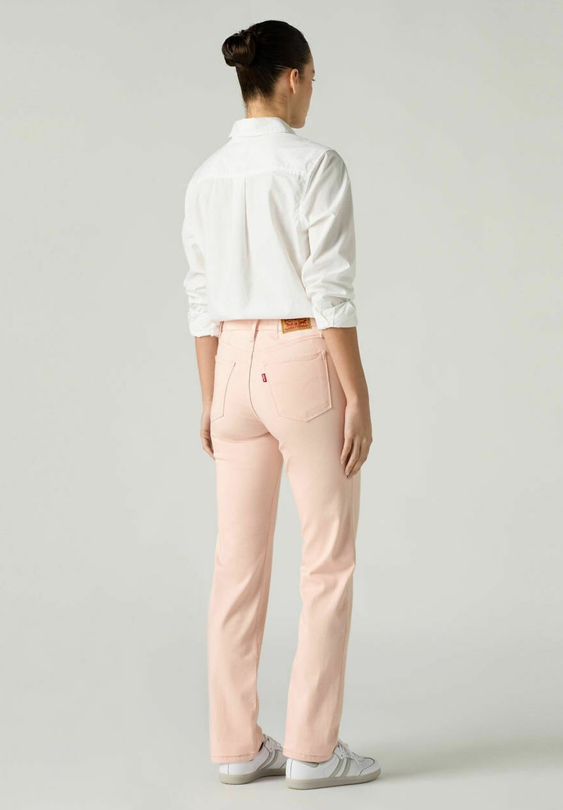 Chemise à col blanc, jean rose clair avec deux poches arrière et une texture subtile. Le modèle porte des baskets blanches. Vue de dos mise en valeur.