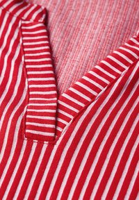 Gestreifter Stoff in Rot und Weiß mit einem V-Ausschnitt. Verfügt über eine strukturierte Oberfläche und eine einfache, saubere Konstruktion ohne zusätzliche Verzierungen.