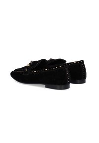 Mocasines de ante negro con acentos de tachuelas en tonos dorados, suela plana y punta redondeada. Presentan un detalle de lazo decorativo en la parte delantera.