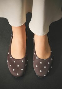 Braune Ballerinas mit Pünktchenmuster, glatter Textur und abgerundetem Zehendesign, kombiniert mit einem hellfarbenen Kleid mit geschwungenem Saum.